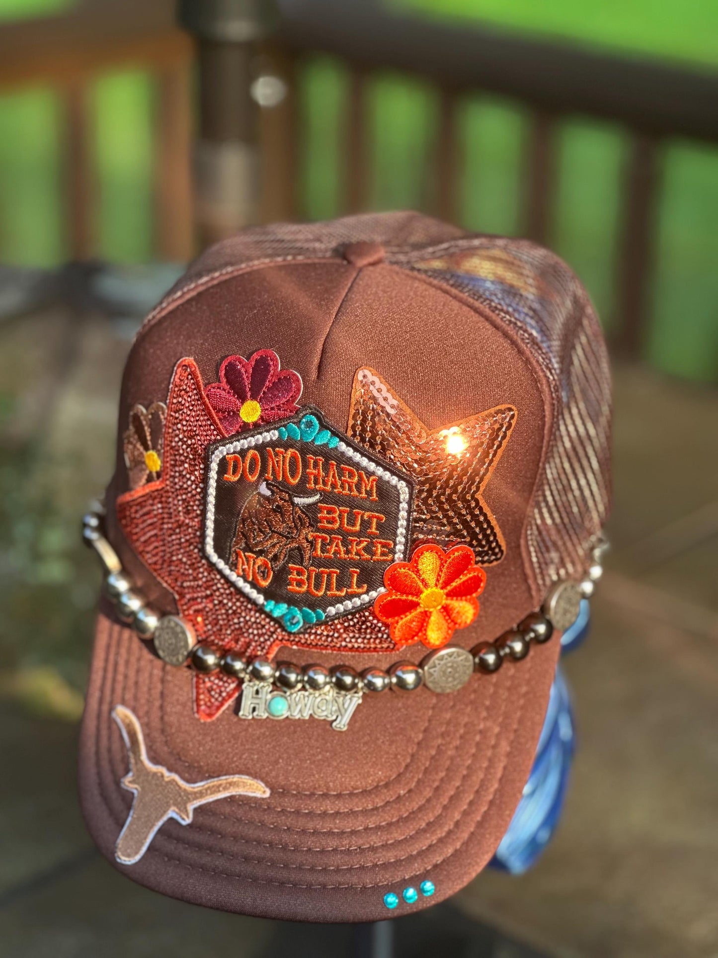 Brown “Do No Harm But Take No Bull” trucker hat with howdy hat chain, ornate teal rhinestones.