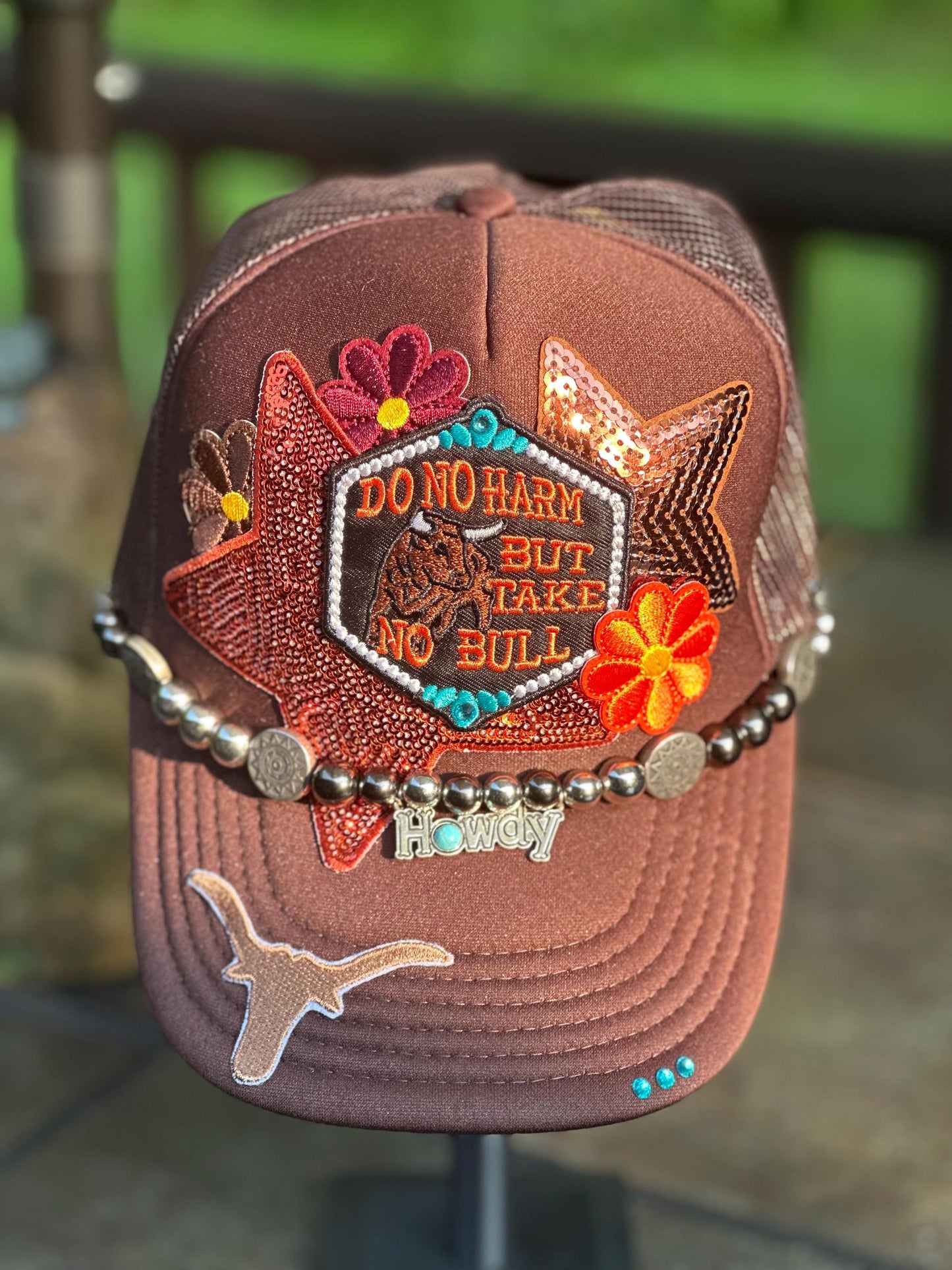 Brown “Do No Harm But Take No Bull” trucker hat with howdy hat chain, ornate teal rhinestones.