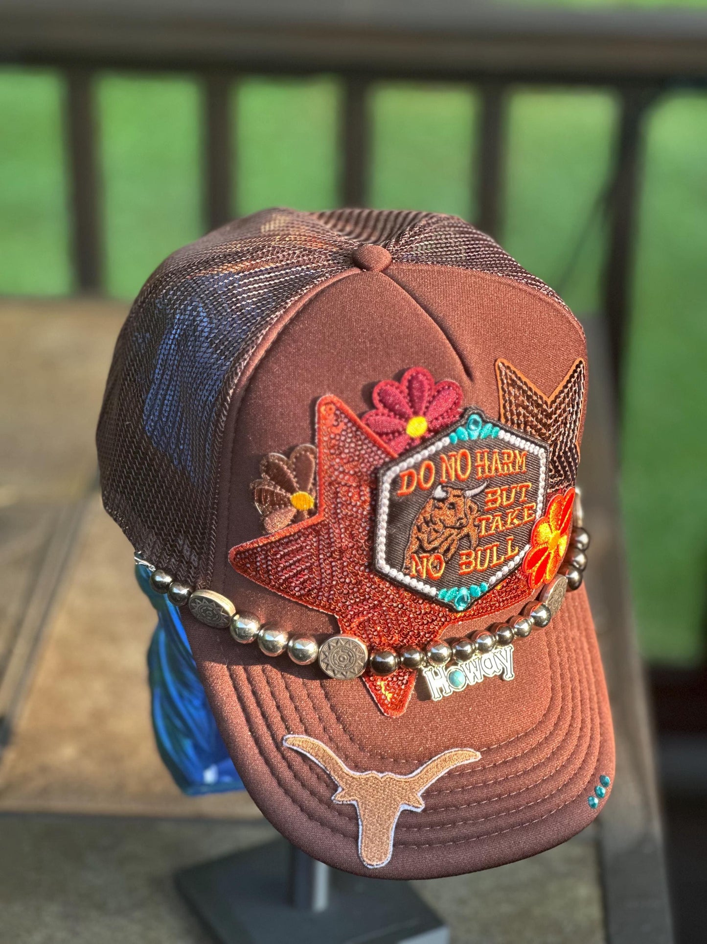 Brown “Do No Harm But Take No Bull” trucker hat with howdy hat chain, ornate teal rhinestones.